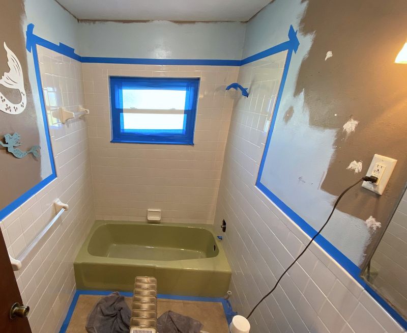 A bathroom before work: an avocado-green tub, painter’s tape around the tile, and patched walls.