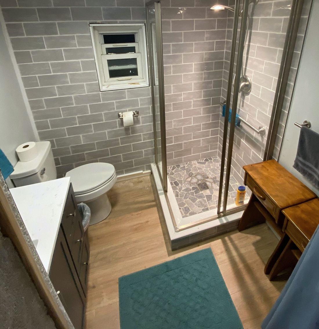 A finished bathroom with a glass corner shower, gray wall tile, and wood-look flooring.
