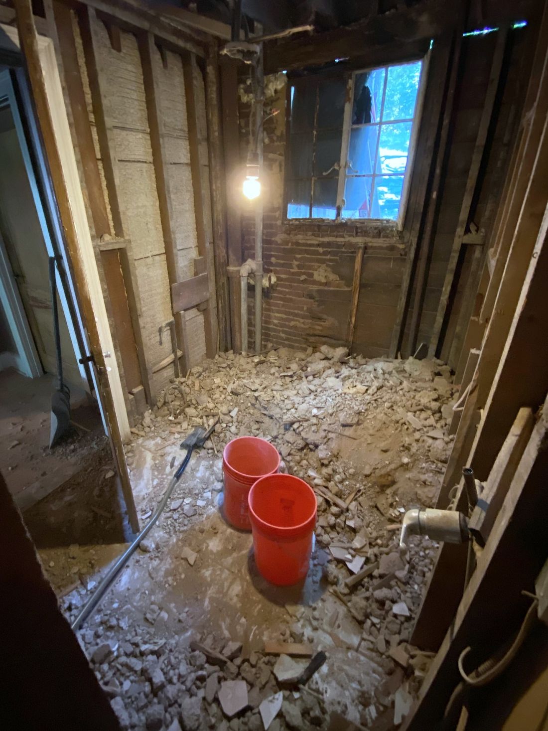 A room stripped to the studs, with broken-up flooring piled on the floor beside two red buckets.