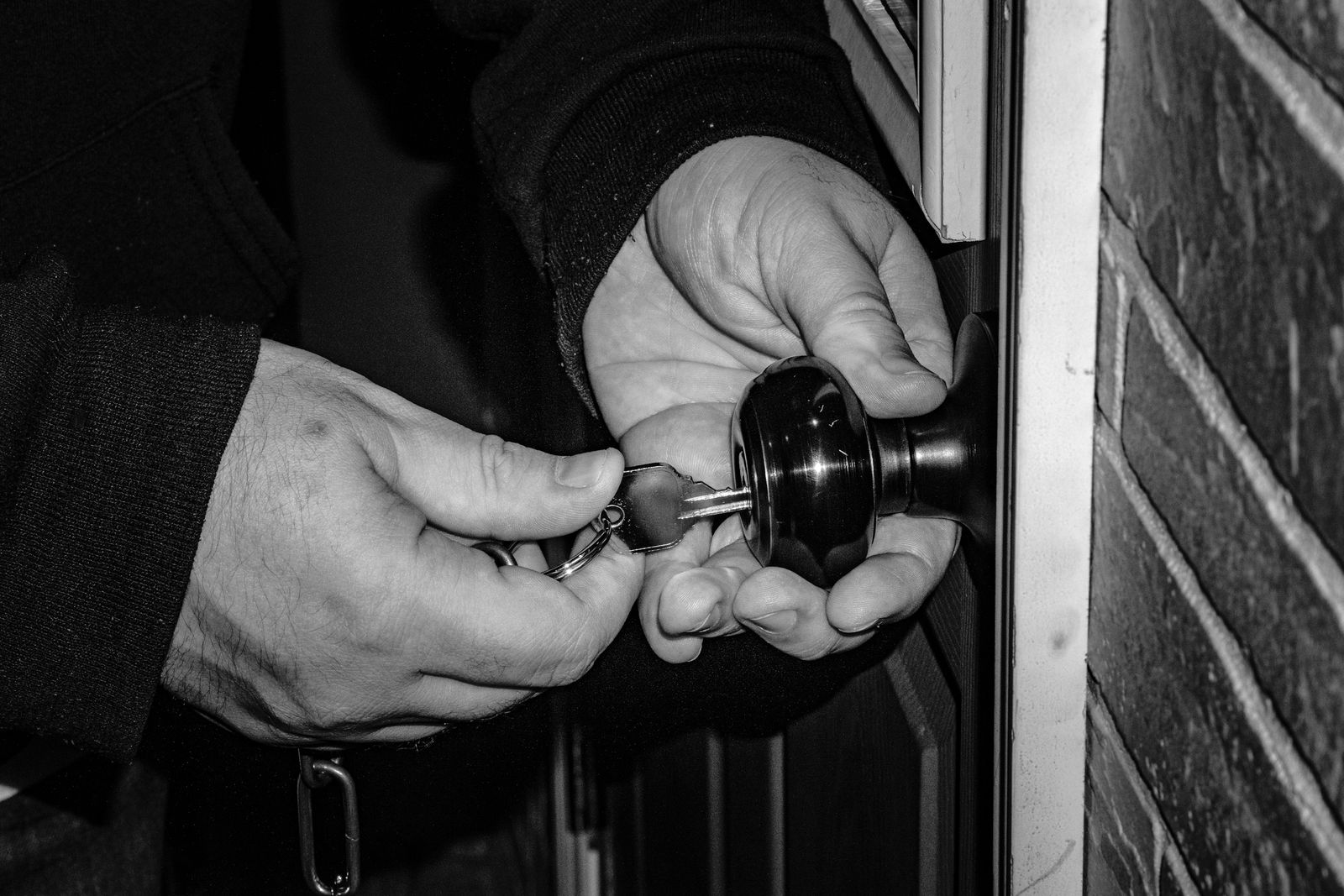 Hands working at a door knob, in black and white.